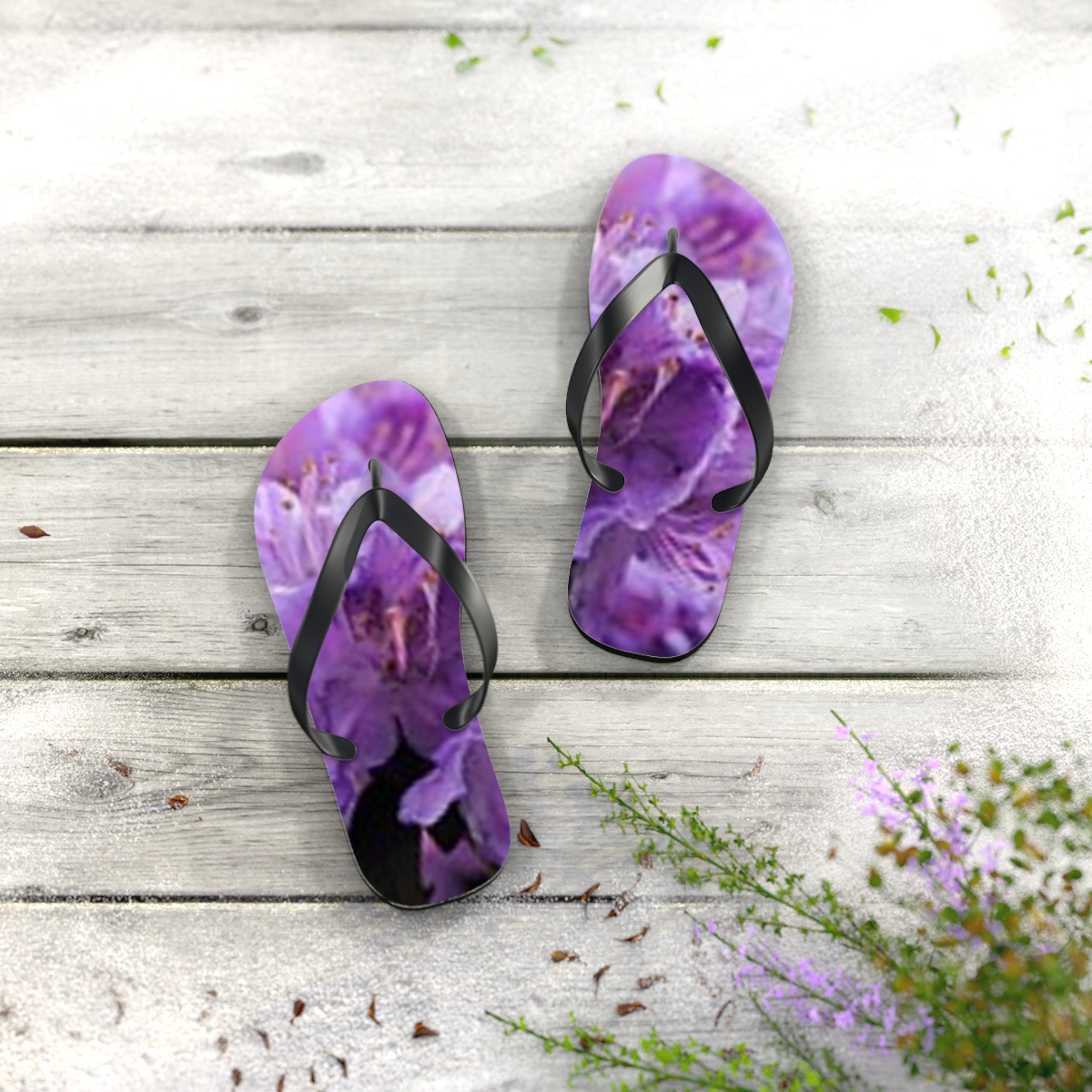Purple floral flip-flops on a weathered wood surface with scattered petals.